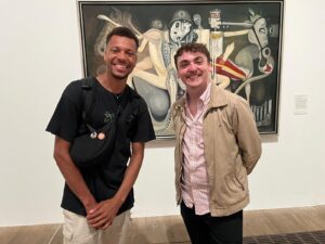 Two SurvivorsUK clients stand smiling next to a painting at a gallery on a cultural trip