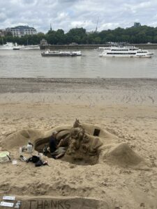 A man carves sculptures into sand on the river Thames
